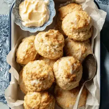 Ultimate Sourdough Discard Scones Recipe 4 Golden Sourdough Discard Scones drizzled with white icing, served with clotted cream in a rustic enamel dish.