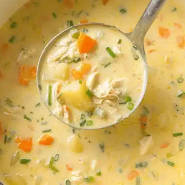 The Ultimate Chicken Potato Soup Recipe 3 Ladle scooping creamy, chunky homemade chicken potato soup with carrots and fresh herbs from a Dutch oven.