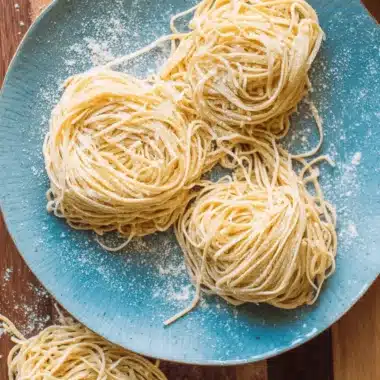 Amazing Sourdough Discard Pasta Made Simple 4 Freshly made Sourdough Discard Pasta spaghetti arranged in three flour-dusted nests on a textured blue ceramic plate.