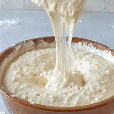 Unlock the Magic: Easy Sourdough Starter Recipe 4 Active, bubbly sourdough starter being lifted by a wooden spoon, illustrating a key step in the Sourdough Starter Recipe process.