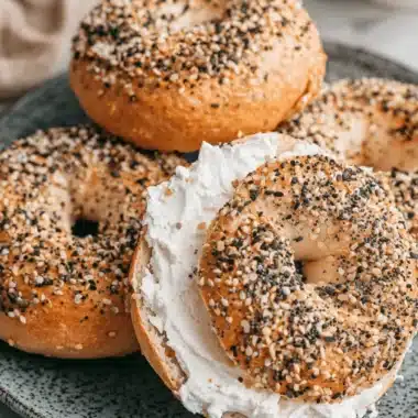 Perfect Sourdough Bagels: Homemade Bliss 3 Close-up of everything Sourdough Bagels on a dark gray plate, one sliced open with a thick spread of cream cheese.