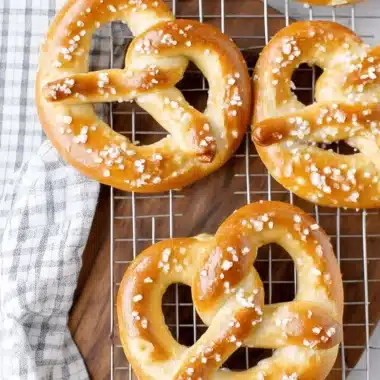 Irresistibly Soft Sourdough Pretzels Recipe 4 Four glossy, golden-brown Soft Sourdough Pretzels sprinkled with coarse salt on a cooling rack.