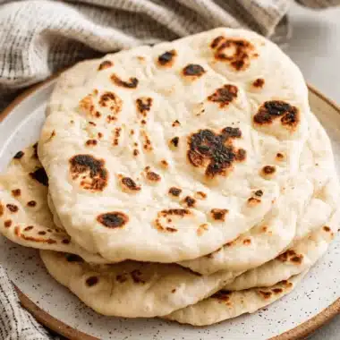 Amazing Sourdough Naan: Easy Homemade Flatbread 3 Stack of freshly made, golden-brown Sourdough Naan with perfect charring on a speckled ceramic plate.