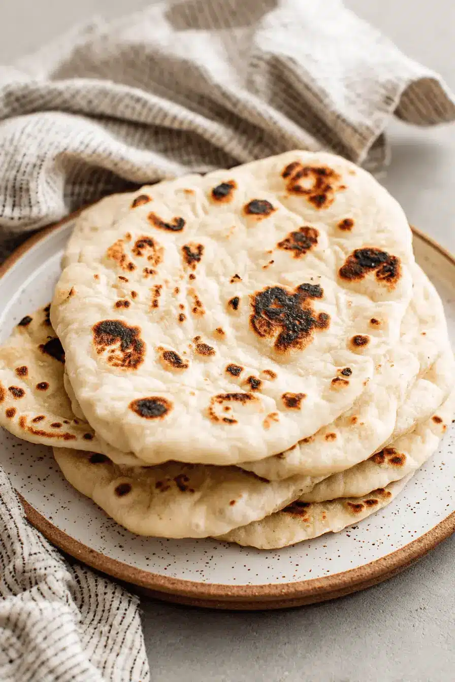 Amazing Sourdough Naan: Easy Homemade Flatbread 2 Stack of freshly made, golden-brown Sourdough Naan with perfect charring on a speckled ceramic plate.