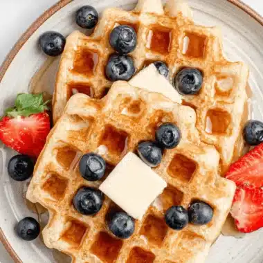 Ultimate Sourdough Waffles: Crispy & Fluffy Recipe 3 Stack of golden-brown Sourdough Waffles topped with syrup, melting butter, blueberries, and fresh sliced strawberries.