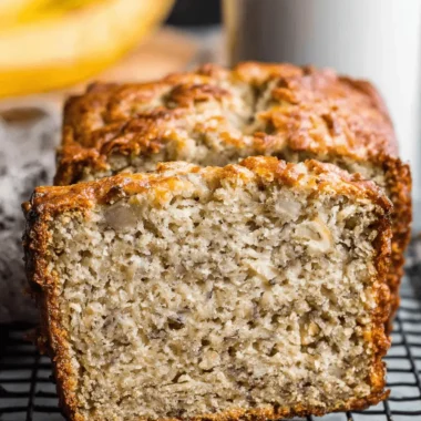 Ultimate Paleo Banana Bread: Easy & Moist 4 Slice of moist paleo banana bread cooling on a black wire rack, with whole bananas in the background.
