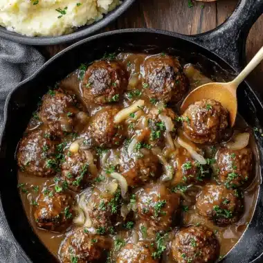 Amazing Salisbury Steak Meatballs in 40 Minutes 3 Cast-iron skillet with rich brown gravy, plump salisbury steak meatballs, and mashed potatoes garnished with parsley.