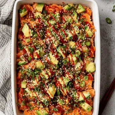 Fantastic Salmon Sushi Bake Recipe 3 Delicious, creamy salmon sushi bake recipe presented in a white baking dish, topped with fresh avocado, scallions, and sriracha.