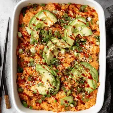 Amazing Salmon Sushi Bake Recipe 3 Baked salmon sushi bake recipe displayed in a white casserole dish, garnished with sliced avocado, green onions, and savory glaze.