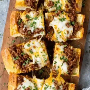 The Ultimate Italian Garlic Bread Sloppy Joes 3 Slices of cheesy italian garlic bread sloppy joes piled on a wooden cutting board, ready for serving.