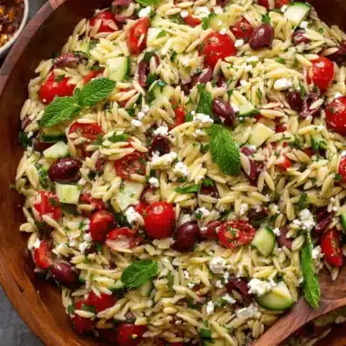 Vibrant Greek Orzo Salad: Simple & Flavorful 3 Overhead close-up of a vibrant greek orzo salad in a rustic wooden bowl with feta, Kalamata olives, and fresh mint.