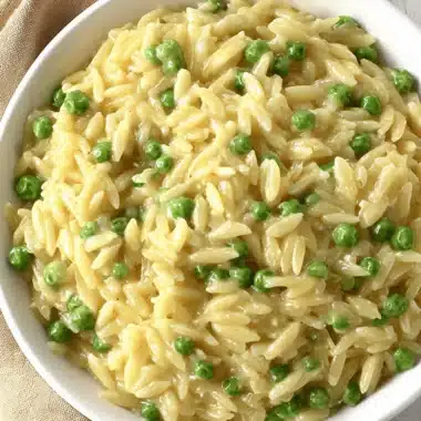 Ultimate Creamy Parmesan Orzo and Peas 3 Close-up, overhead shot of a creamy bowl of parmesan orzo and peas served on a wooden surface.