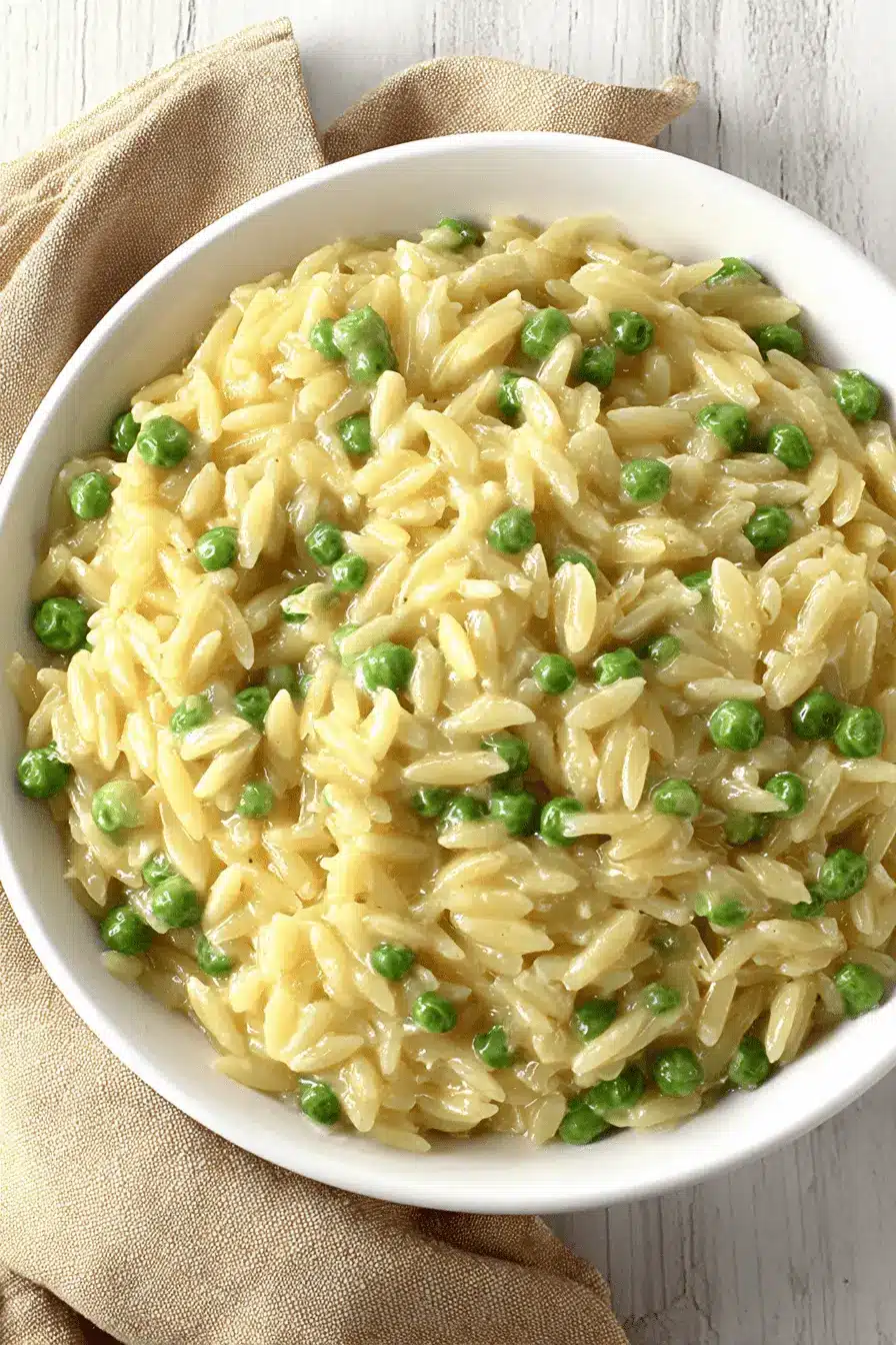 Ultimate Creamy Parmesan Orzo and Peas 2 Close-up, overhead shot of a creamy bowl of parmesan orzo and peas served on a wooden surface.