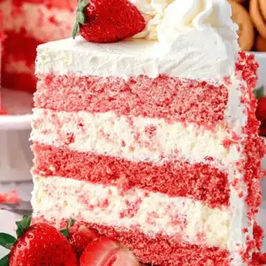 Ultimate Strawberry Crunch Cheesecake 4 A slice of layered strawberry crunch cheesecake on a light pink plate, garnished with a whole strawberry and surrounded by fresh fruit.