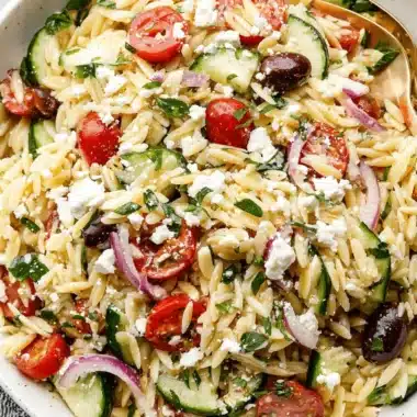 Vibrant Mediterranean Orzo Salad Recipe 4 A vibrant close-up of a bowl of fresh mediterranean orzo salad topped with feta cheese, Kalamata olives, and cherry tomatoes.