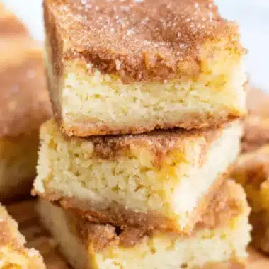 Quick & Easy Cinnamon Sugar Blondies: Irresistibly Chewy 3 Stacked homemade Cinnamon Sugar Blondies on a wooden cutting board, showing the cinnamon swirl topping and caramelized edges.