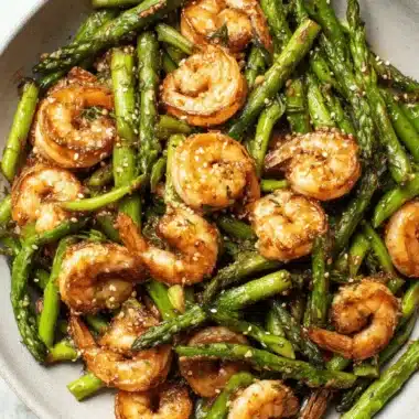 Ultimate Shrimp and Asparagus Stir Fry 3 Plump, glossy, pan-seared shrimp and asparagus stir fry coated in a savory dark sauce and topped with sesame seeds in a rustic bowl.