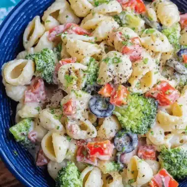 Amazing Creamy Pasta Salad: Your New Favorite Dish 4 Delicious Creamy Pasta Salad with shell pasta, broccoli, tomatoes, and black olives in a dark blue bowl.