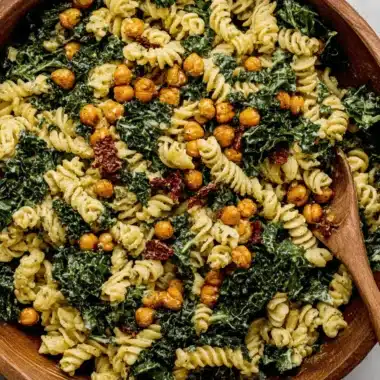 Ultimate Kale Pasta Caesar Salad 4 Creamy fusilli pasta salad featuring fresh chopped kale, roasted chickpeas, and sun-dried tomatoes. This vibrant kale pasta caesar salad is served in a rustic wooden bowl.