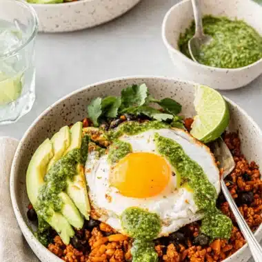 Amazing Breakfast Burrito Bowl Recipe 4 Overhead view of a vibrant breakfast burrito bowl with a fried egg, avocado, black beans, and green sauce in a rustic ceramic bowl.
