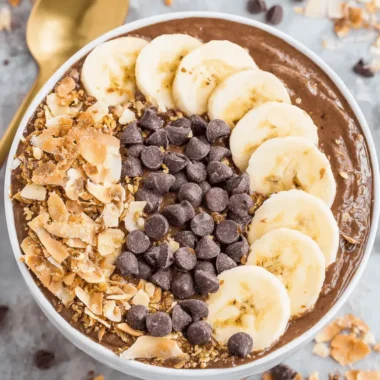 The Ultimate Chunky Monkey Smoothie Bowls 4 Overhead shot of thick chocolate Chunky Monkey Smoothie Bowls topped with banana slices, dark chocolate chips, and toasted coconut flakes.