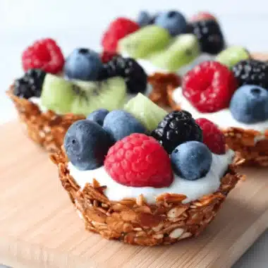 The Ultimate Breakfast Granola Cups Recipe 3 Two healthy yogurt and berry parfaits nestled in crispy homemade Breakfast Granola Cups on a light wooden board.