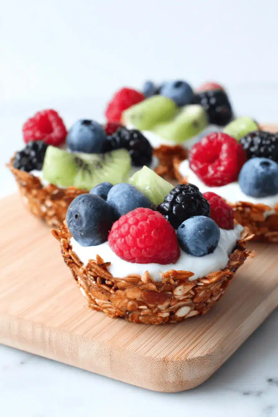 The Ultimate Breakfast Granola Cups Recipe 2 Two healthy yogurt and berry parfaits nestled in crispy homemade Breakfast Granola Cups on a light wooden board.