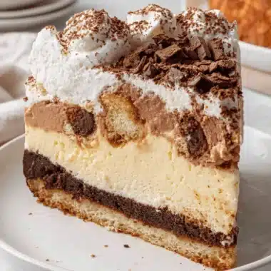 Ultimate No-Bake Tiramisu Cheesecake 3 Decadent slice of layered tiramisu cheesecake topped with chocolate shavings and whipped cream on a white plate.