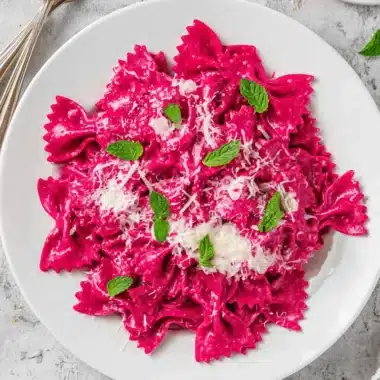 Vibrant & Easy Beet Pasta with Creamy Ricotta 4 Elegant serving of vibrant pink farfalle Beet Pasta garnished with fresh mint and grated cheese.