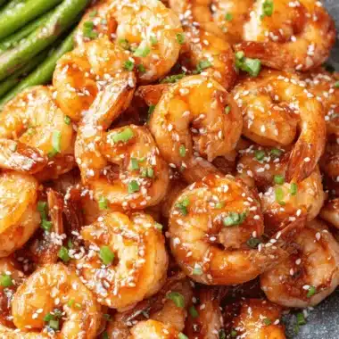 Amazing Sriracha Shrimp: Sweet & Spicy in 20 Mins 3 Overhead shot of glossy, glazed sriracha shrimp topped with sesame seeds and green onions, plated next to vibrant green asparagus.