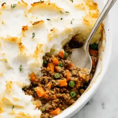 Ultimate Comfort Shepherd's Pie Recipe 4 Overhead view of a baked shepherd's pie recipe with golden, swirled mashed potatoes and a spoon serving the rich meat and vegetable filling.