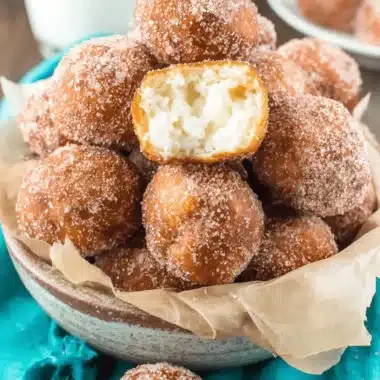 Foolproof Donut Holes Recipe: Easy No-Yeast Treats 3 Golden-brown, sugar-coated donut holes piled high in a rustic bowl, with one broken to show the creamy filling, illustrating a successful donut holes recipe.