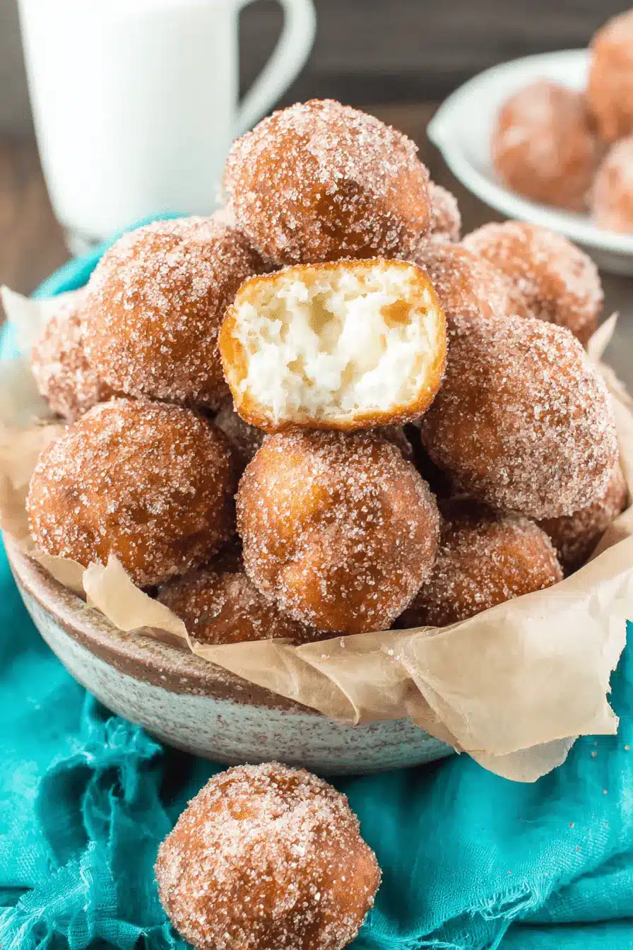 Foolproof Donut Holes Recipe: Easy No-Yeast Treats 2 Golden-brown, sugar-coated donut holes piled high in a rustic bowl, with one broken to show the creamy filling, illustrating a successful donut holes recipe.