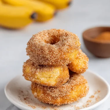 Amazing Easy Banana Donut Holes in 20 Minutes 4 Stack of golden cinnamon-sugar donuts on a white plate, representing a recipe for homemade banana donut holes.