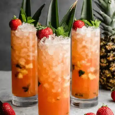 The Ultimate Strawberry Pineapple Mojito 3 Three tall glasses of vibrant, crushed-ice Strawberry Pineapple Mojito garnished with fresh strawberries, mint sprigs, and pineapple leaves.