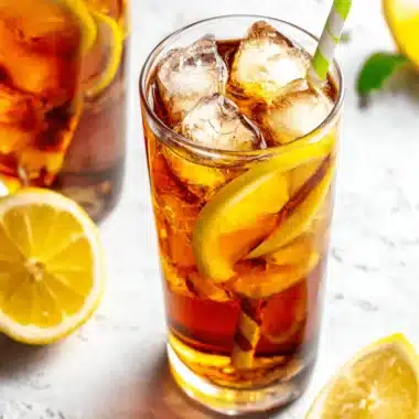 Amazing Smooth Ice Lemon Tea Recipe 4 Two glasses of chilled Ice Lemon Tea garnished with fresh lemon slices and mint, shot from a high angle on a textured surface.