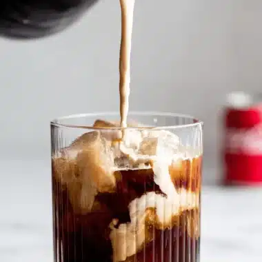 The Ultimate Dirty Soda Recipes for Delicious Sips 4 Close-up of thick cream swirling into iced coffee in a ribbed glass, demonstrating the mixing technique used for smooth dirty soda recipes.