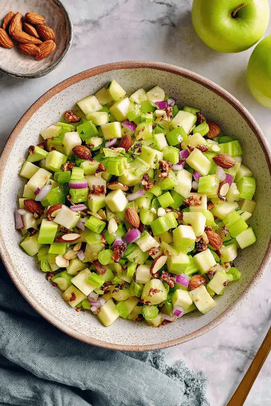 Amazing Celery Salad: Quick & Easy Recipe 2 Crisp celery salad featuring diced green apples, red onion, and whole almonds in a speckled ceramic bowl.