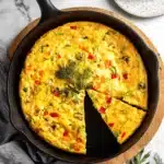Wonderful Weeknight Frittata Recipe 9 Golden vegetable frittata recipe in a black cast iron skillet with a slice removed onto a white plate.