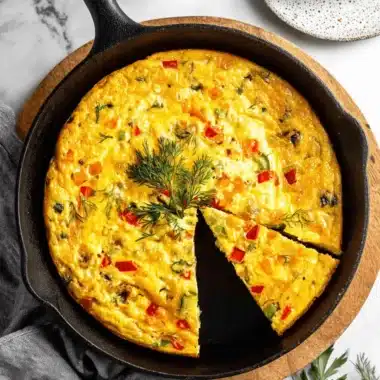 Wonderful Weeknight Frittata Recipe 3 Golden vegetable frittata recipe in a black cast iron skillet with a slice removed onto a white plate.