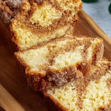 Amazing Easy Amish Cinnamon Bread Recipe 3 Sliced loaf of freshly baked amish cinnamon bread dusted with sugar on a rustic wooden board.