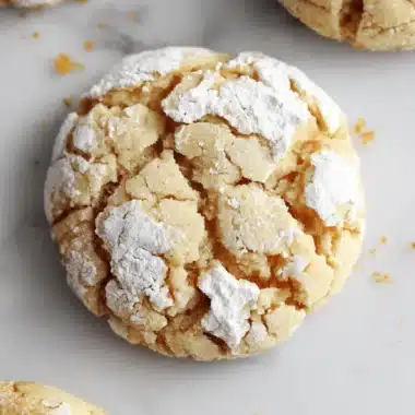 Magic Brown Butter Cinnamon Crinkle Cookies 4 Close-up of golden-brown brown butter cinnamon crinkle cookies dusted heavily with powdered sugar on white marble.