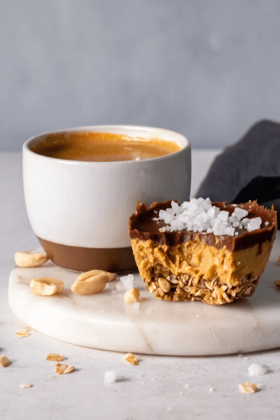 Amazing Foolproof No Bake Peanut Butter Oat Cups 2 Close-up of a single bitten no bake peanut butter oat cup topped with sea salt, presented next to a coffee mug.