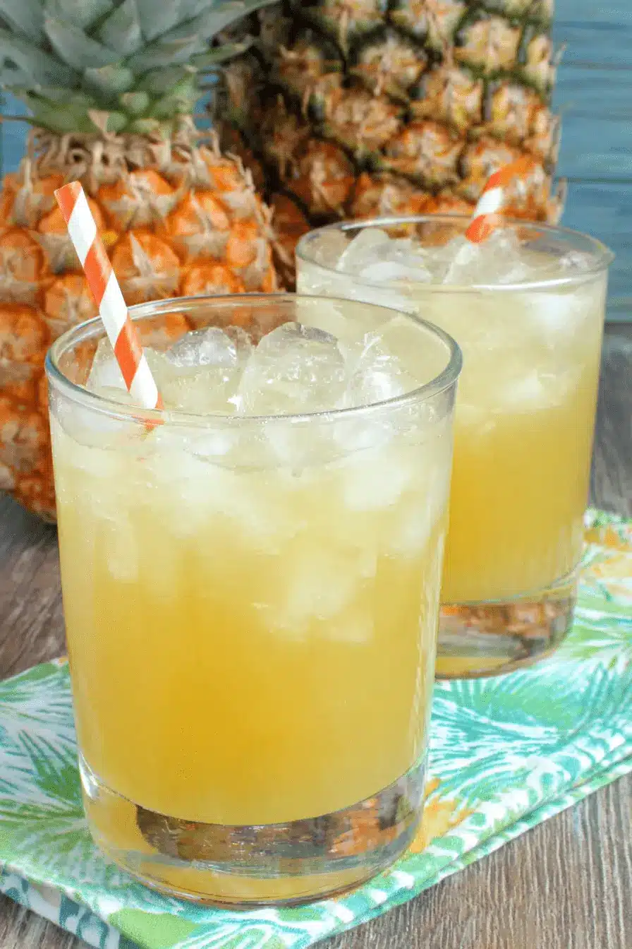 Easy Pineapple Lemonade Punch for Any Crowd 2 Two glasses of frothy pineapple lemonade punch served over ice with festive striped straws next to fresh pineapples.