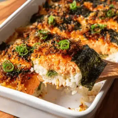 Amazing Salmon Sushi Bake Recipe 3 Close-up of a layered, golden-crusted salmon sushi bake recipe being served from a white baking dish.