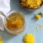 Magic Dandelion Jelly Recipe: Capture Sunshine 5 Jar of homemade amber dandelion jelly with a spoon and loose petals, representing a successful dandelion jelly recipe.