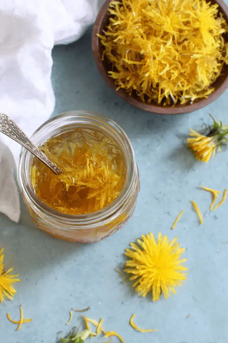Magic Dandelion Jelly Recipe: Capture Sunshine 2 Jar of homemade amber dandelion jelly with a spoon and loose petals, representing a successful dandelion jelly recipe.