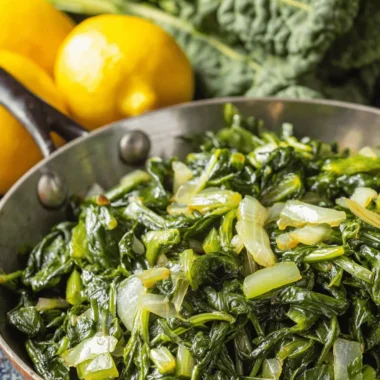 Simple Dandelion Greens Recipe: Fast & Flavorful 3 Cooked dandelion greens recipe with wilted onions in a copper skillet, ready to serve alongside fresh lemons.