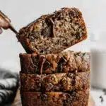 Ultimate Moist Chocolate Chip Banana Bread 7 Three moist slices of Chocolate Chip Banana Bread stacked on a wooden board, drizzled with chocolate sauce, with one slice being lifted.