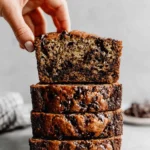 Unbelievably Moist Chocolat Banana Bread 5 Hand reaching for a slice of moist, stacked chocolat banana bread with dark chocolate chips.